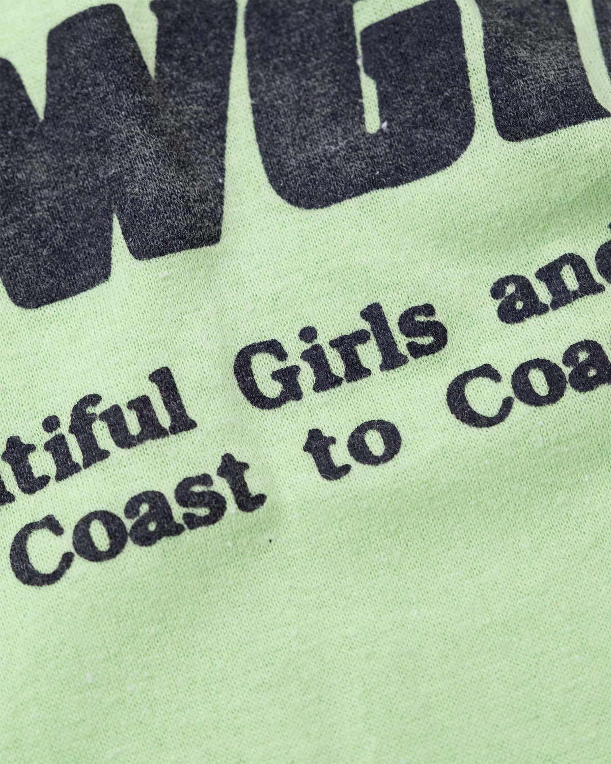 Close-up of coast-to-coast slogan text on vintage Deja Vu Showgirls T-shirt.